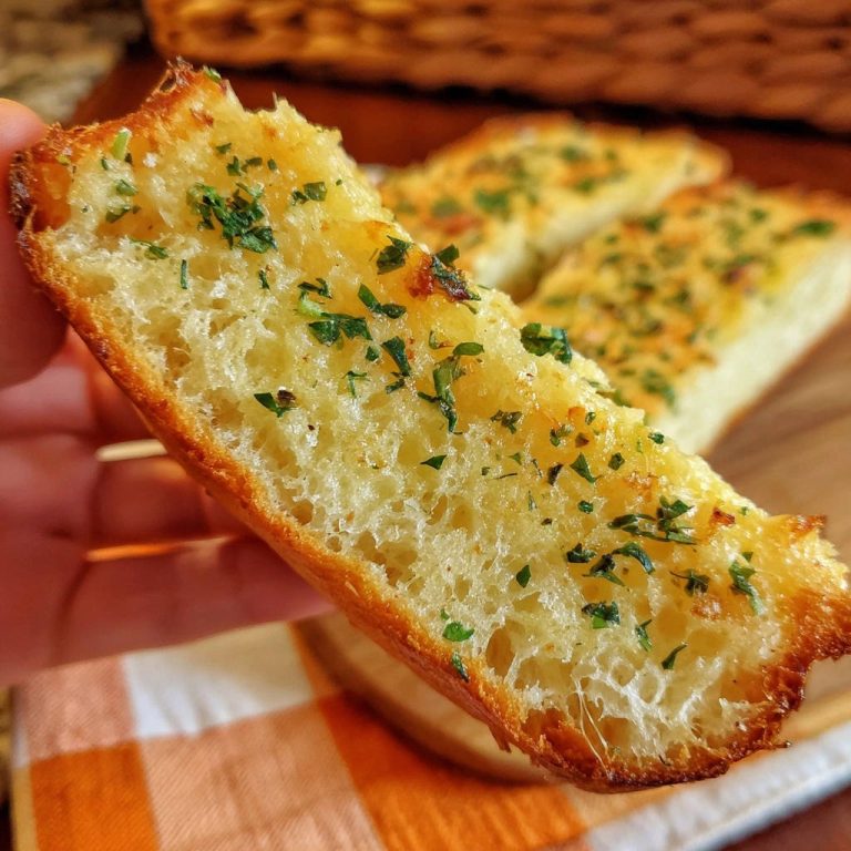 Hausgemachtes Knoblauchbrot, ein angeschnittenes Stück zeigt die fluffige Textur und die knusprige Kruste mit Petersilie bestreut.