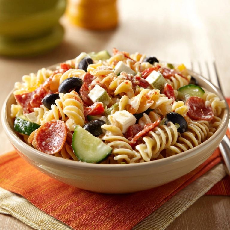 Sommerlicher Fusilli-Salat mit Salami, Oliven und Feta, nahaufnahme in einer Schüssel auf einem orangefarbenen Tuch.