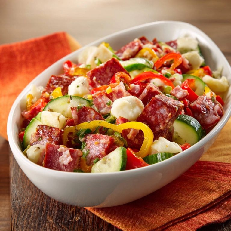 Herzhafter Salami-Nudelsalat in einer weißen Schüssel, Nahaufnahme der Zutaten mit Salami, Gemüse und Käsebällchen.
