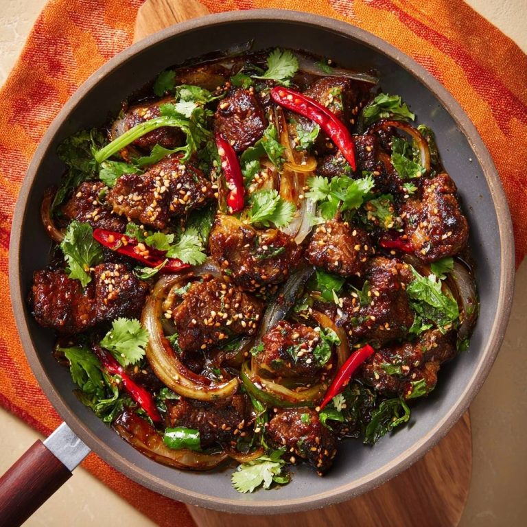 Scharfes Chili-Rindfleisch aus dem Wok, von oben in einer Pfanne mit Zwiebeln und Koriander garniert.