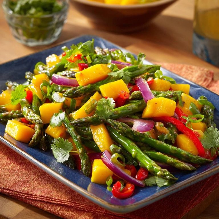 Knackiger Spargel-Mango-Wok serviert auf einer blauen Platte mit roten Zwiebeln und Koriandergarnitur