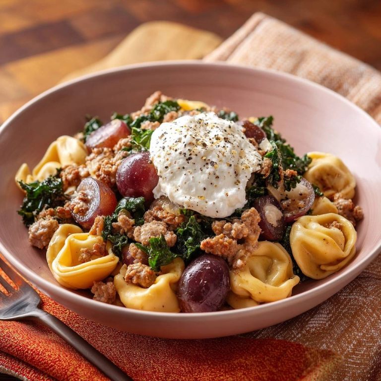 Herbstliche Grünkohl-Tortellini-Pfanne mit Hack, Trauben & Ricotta, serviert in einer Schüssel mit cremiger Ricotta-Haube und Pfeffer.