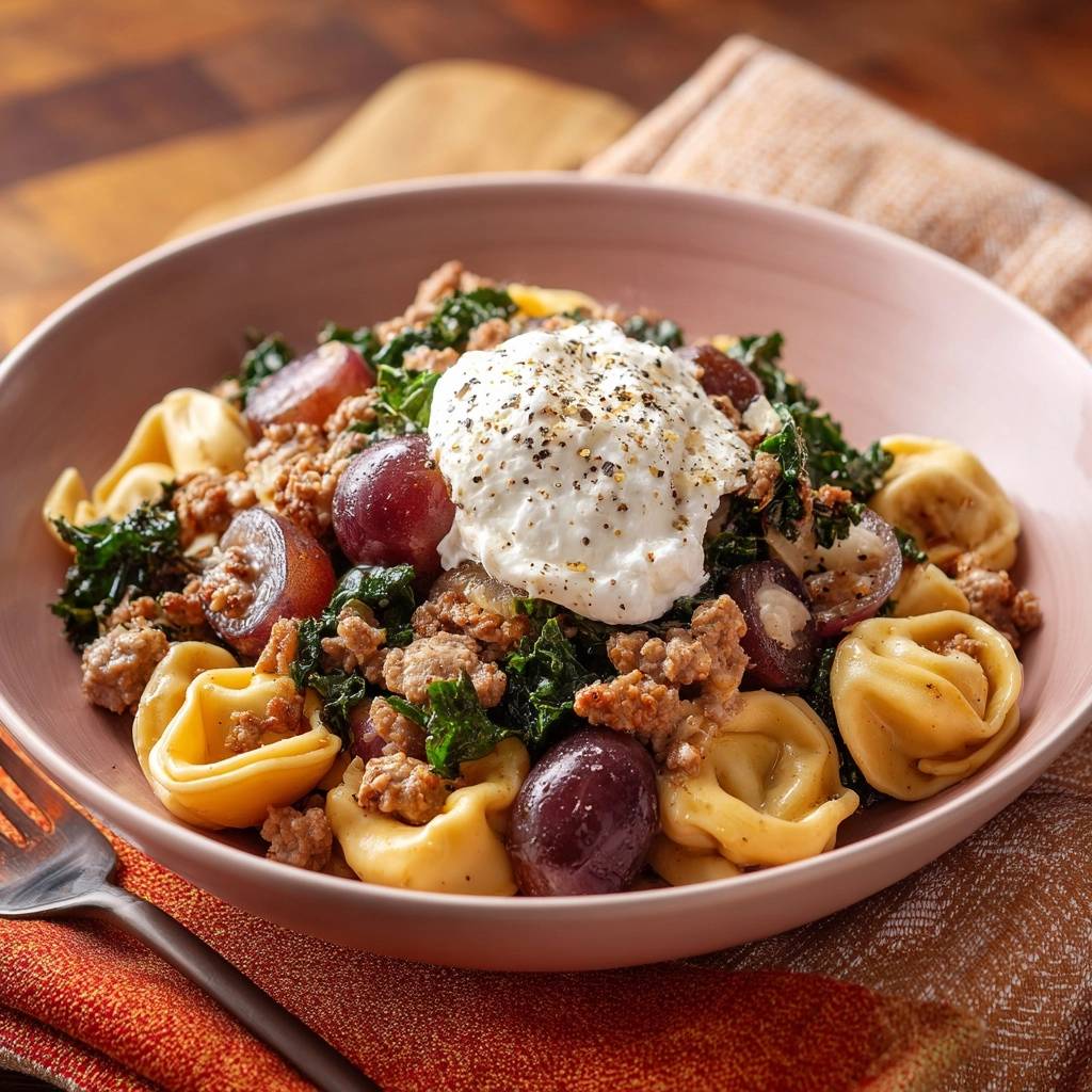 Herbstliche Grünkohl-Tortellini-Pfanne mit Hack, Trauben & Ricotta, serviert in einer Schüssel mit cremiger Ricotta-Haube und Pfeffer.