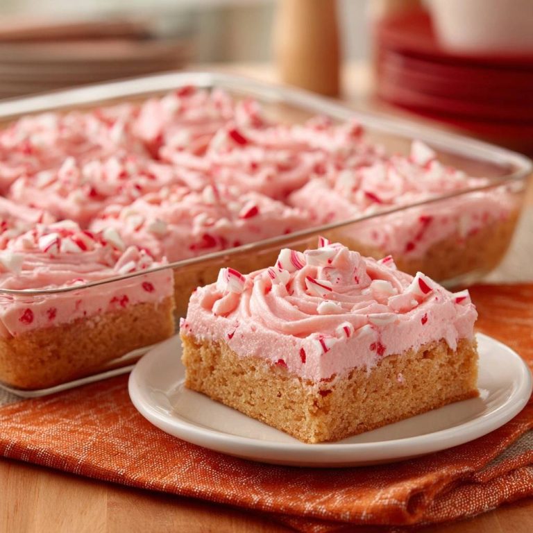 Pfefferminz-Blechkuchen angeschnitten auf einem Teller, mit zarter rosa Zuckerguss-Haube und zerstoßenen Pfefferminzbonbons garniert.