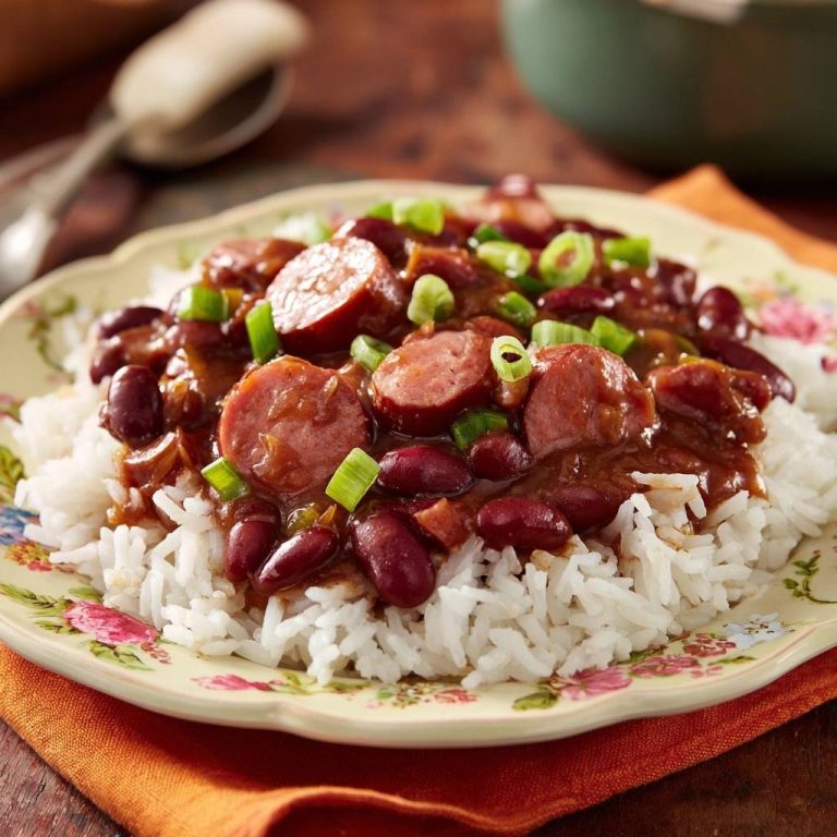 Herzhaftes Red Beans and Rice mit Wurst und Frühlingszwiebeln, serviert auf einem Teller mit Reis und einer cremigen Sauce.