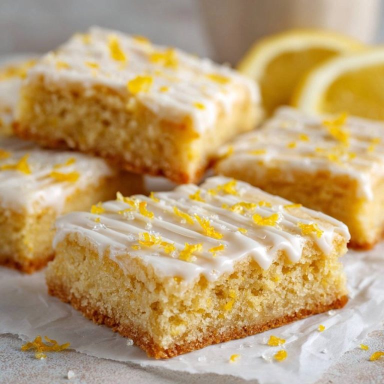 Saftige Zitronen-Schnitten mit Zuckerguss und frischer Zitronenschale garniert, Nahaufnahme des Gebäcks.
