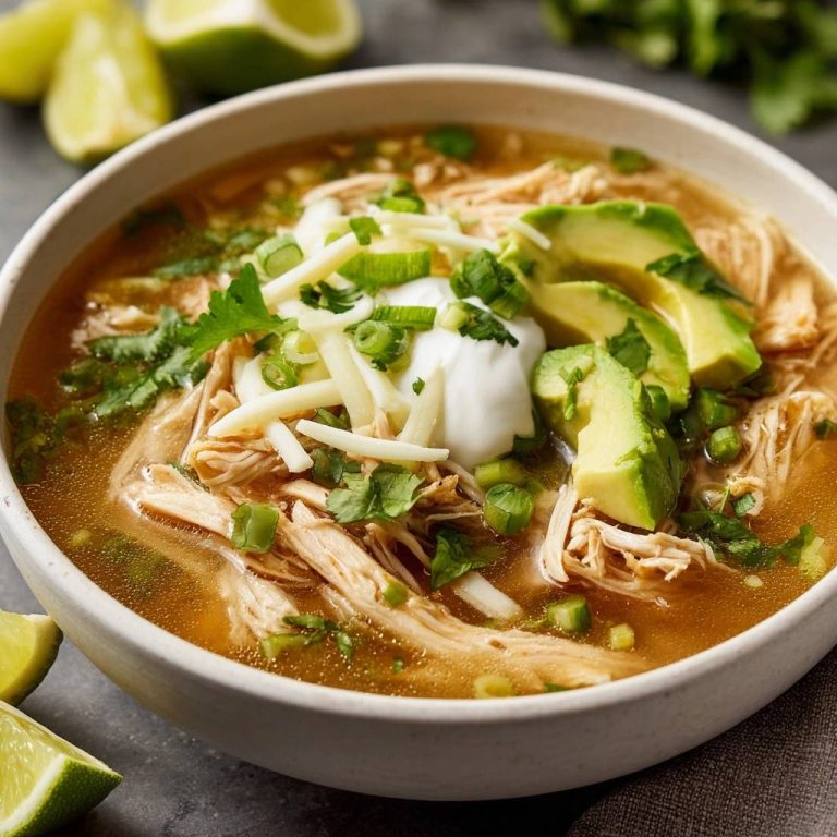 Würzige Limetten-Hähnchensuppe, garniert mit Avocado, Sauerrahm, Käse und Koriander, serviert in einer Schüssel mit Limettenspalten.